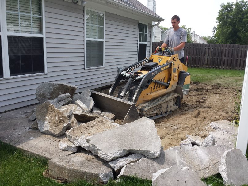 Demolition & Removal A small skid loader is demolishing and removing a previous patio to prepare for a replacement one.