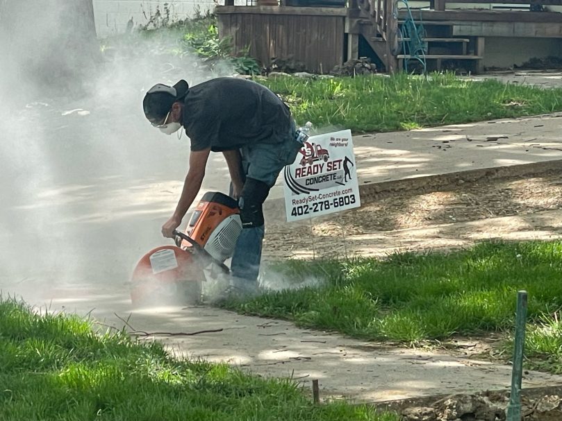 New Concrete Sidewalk Worker drilling into concrete to prepare for a new sidewalk, surrounded by dust and debris. The worker is using a power tool