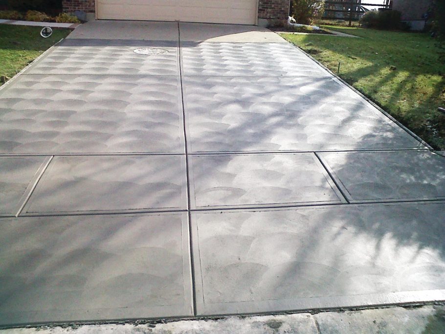 New driveway with half U-shaped rounded designs embedded in the concrete surface. The driveway features a smooth, freshly poured surface