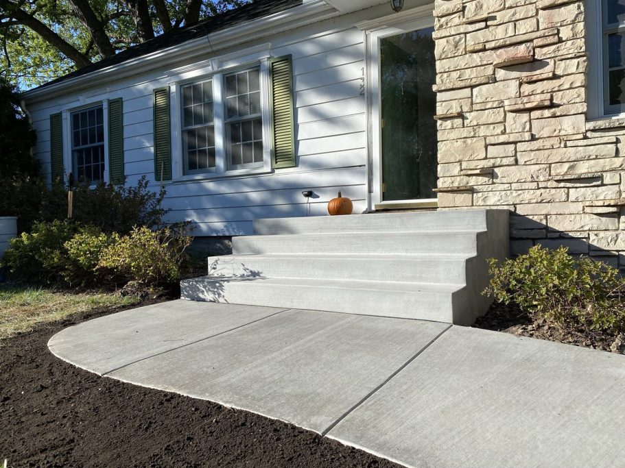 Four wide new smooth concrete stairs leading up to a home’s front entryway. 